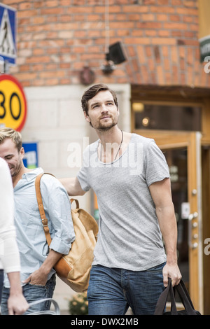 Nachdenklicher Mann Tragetasche bei einem Spaziergang mit Freunden im freien Stockfoto