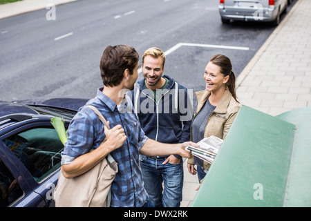 Glückliche Freunde mit Mann, der Zeitung in Recyclingbehälter Stockfoto