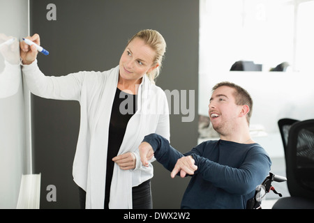 Geschäftsfrau, die während der Arbeit mit behinderten Geschäftsmann im Büro auf Whiteboard schreiben Stockfoto