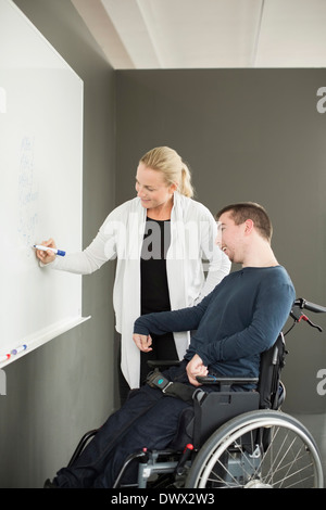 Geschäftsfrau, die während der Arbeit mit behinderten Geschäftsmann im Büro auf Whiteboard schreiben Stockfoto