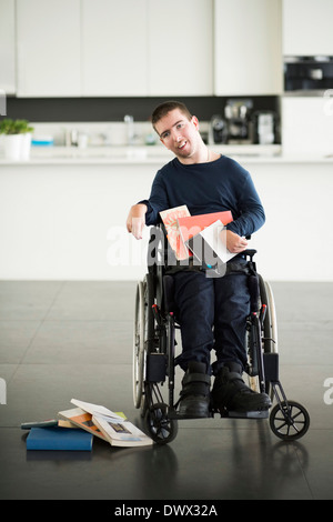 Porträt des behinderten Menschen mit Büchern auf Rollstuhl zu Hause Stockfoto