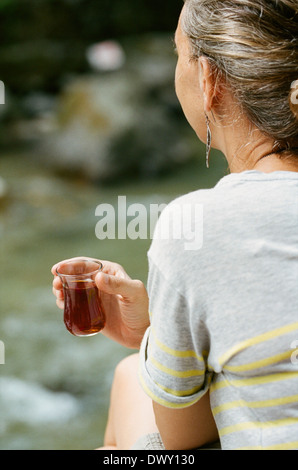 Frau mit Getränk im Freien sitzen und wegsehen Stockfoto
