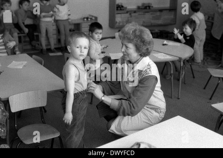 Berlin, DDR, Lehrer in einem Kindergarten hängt eine kleine Jungen-Kleidung Stockfoto