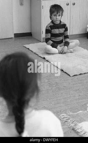 Berlin, DDR, sitzt ein kleiner Junge im Kindergarten gelangweilt sitzen mit gekreuzten Beinen auf dem Boden Stockfoto