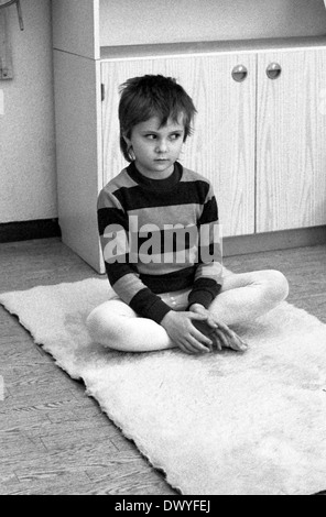 Berlin, DDR, sitzt ein kleiner Junge im Kindergarten unsicher im Schneidersitz auf dem Boden Stockfoto