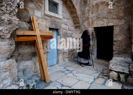 Ein äthiopisch-orthodoxe Christ steht neben Kreuzungen, die den Ort der 10. Kreuzungsstation nahe dem Eingang zur äthiopisch-orthodoxen Kammer am Parvis oder Parvise der Grabeskirche in der christlichen Viertel-Altstadt von Ostjerusalem Israel markieren Stockfoto