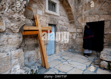 Ein äthiopisch-orthodoxe Christ steht neben Kreuzungen, die den Ort der 10. Kreuzungsstation nahe dem Eingang zur äthiopisch-orthodoxen Kammer am Parvis oder Parvise der Grabeskirche in der christlichen Viertel-Altstadt von Ostjerusalem Israel markieren Stockfoto