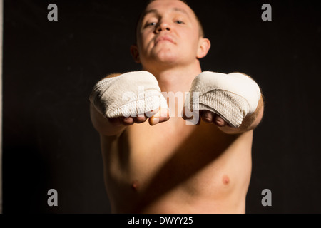 Junge Boxer Verlängerung beider bandagierte Fäuste in die Kamera, als er seine Hände nach einem Kampf mit Schwerpunkt bereitet Stockfoto