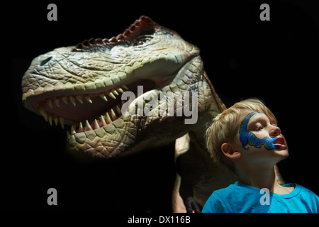 Kind blonde junge Spaß mit realen Modell des Tyrannosaurus Rex Dinosaurier - in der Größe eines menschlichen Kindes gegenüber Stockfoto