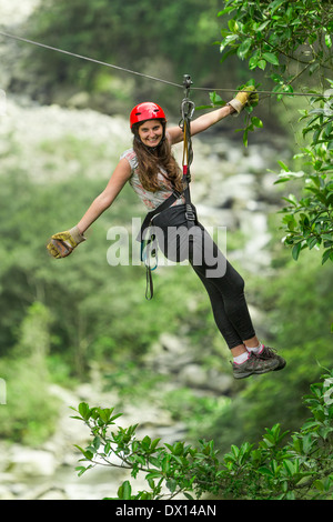 Eine Frau zieht durch einen dichten, grünen Wald. Sie trägt einen roten Helm, ein ärmelloses Oberteil, schwarze Leggings und Wanderschuhe mit weißen Socken. Sie ist mit einem Gurtzeug und gesichert Stockfoto