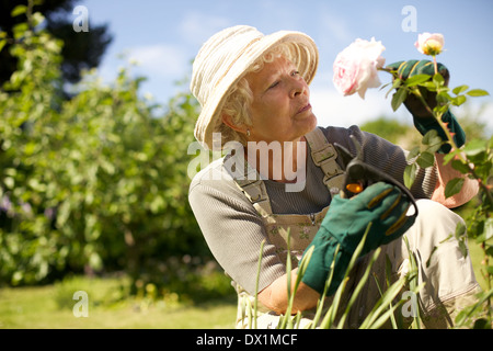 Ältere Frau trägt Sonnenhut Check-Blumen im Garten im Freien. Kopieren Sie Raum.