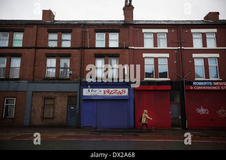 Eine Frau, vorbei an einer verfallenen Ladenzeile im Kensington Bereich von Liverpool. Stockfoto