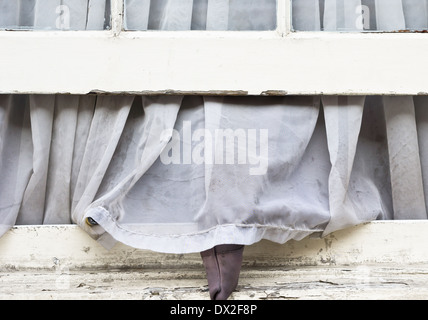 Eine schmutzige Gardine hing aus einem offenen Fenster Stockfoto