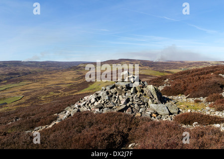 Cairn auf dem Westgipfel Calver Hill mit dem Rauch von Heather brennende Feuer in der Ferne Swaledale Yorkshire Dales UK Stockfoto