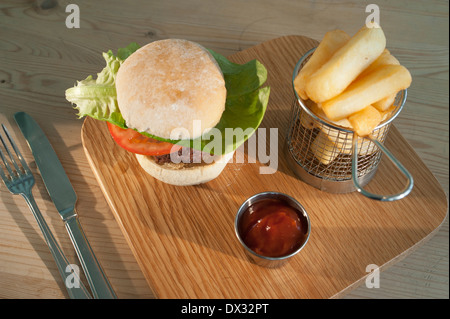 Burger mit Salat Beilage in ein weißes Brot Brötchen mit einer Beilage Pommes Frites und Tomatenketchup serviert auf einer Holzplatte Stockfoto