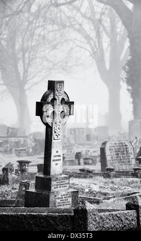 Kreuz Grabstein im Nebel bei Banbury Friedhof mit einem Mann zu Fuß in den Hintergrund, Oxfordshire, England. Monochrom Stockfoto