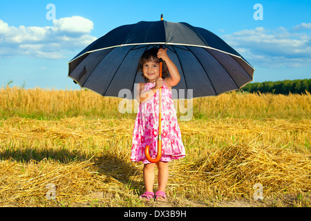 Glückliche kleine Mädchen versteckt unter großen schwarzen Regenschirm bei Schönwetter Stockfoto