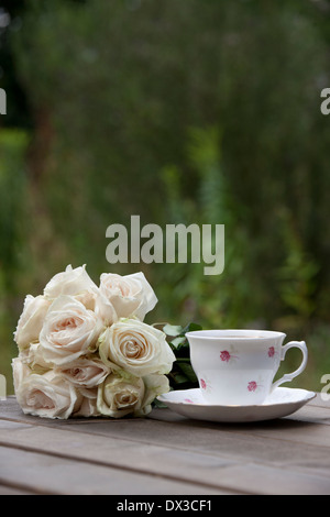 Rosa Rosen und einer Teetasse und Untertasse auf einem Holztisch Stockfoto