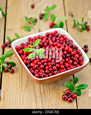 Reife rote Preiselbeeren in einer Schüssel mit einem Zweig mit Beeren und Blätter auf dem Hintergrund der Holzbretter Stockfoto