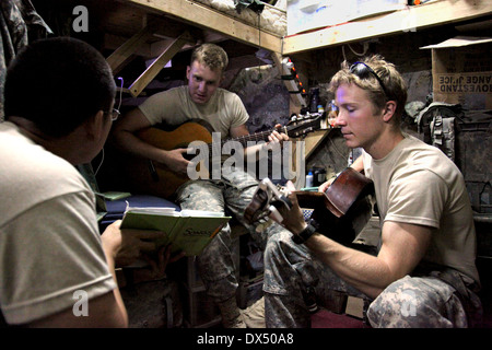 US Army Spc. Paul Yi hält ein Buch von Liedtexten für Pfc. Justin Boone, Center und Sgt. Neil Hawley während sie ihre akustische Gitarren in ihren Wohnbereich auf Combat Outpost Gorbuz 21. Juli 2009 in Gorbuz, Afghanistan spielen. Der Außenposten ist in einer angespannten Lage an der afghanisch - pakistanischen Grenze. Stockfoto