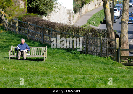 Mann sitzt auf einer Bank und liest eine Zeitung in einem ruhigen Dorf. (Lose Village, Kent, England) Stockfoto