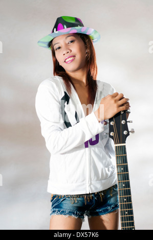 junge asiatische Frau mit Gitarre in Studioumgebung Stockfoto