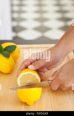 Hände des Mannes schneiden Zitrone in Querschnitt auf Holzbrett in der heimischen Küche, erhöhte Ansicht Stockfoto