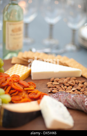 Käse, Cracker, Nüssen, Trauben und Salami auf hölzernen Käseplatte neben Weißwein, Nahaufnahme Stockfoto