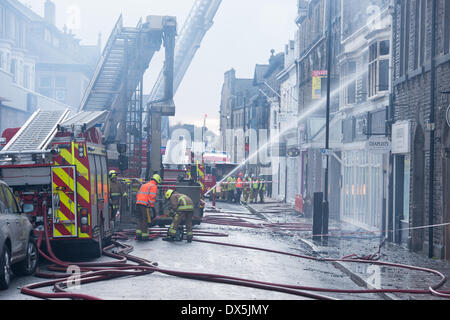 Feuerwehrmänner, die durch Motoren & brennende Gebäude, bekämpfen das Feuer mit Wasser Jet am ausgebrannten, geschwärzte Windows - Harrogate, Yorkshire, England, UK. Stockfoto