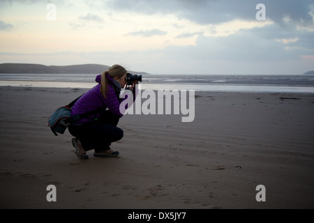 Eine junge Dame, die Aufnahme eines Fotos mit einer DSLR-Kamera an einem Strand in der Dämmerung. Stockfoto