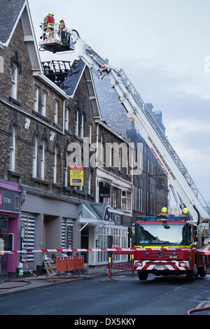 Brave Feuerwehrmänner bis hohe Leiter (2 unten am Motor) prüfen Sie, Schäden an Dach am Zentrum Gebäude - Harrogate, North Yorkshire, England, UK. Stockfoto