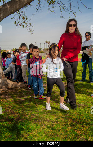 Ein Lehrer führt ihr Amerikaner asiatischer Abstammung, kaukasischen und Hispanic Schüler erste Klasse in der Schlange vor einem Garden Grove, CA, Grundschule Spielplatz. Stockfoto