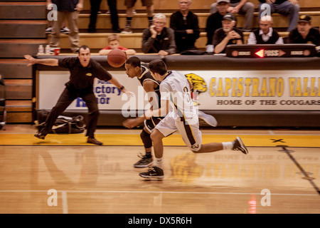 Eine afrikanische amerikanische High-School-Basketball-Spieler dribbelt Vergangenheit ein Gegner als sein Trainer Ermutigung in Mission Viejo, Kalifornien schreit. Stockfoto