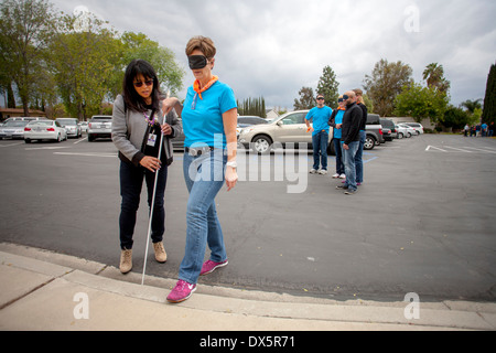 Besucher zu einer Schule für Blinde in Tustin, Kalifornien, werden die Augen verbunden um die es ihnen ermöglichen, Blindheit zu erleben, wie sie lernen, einem Blindenstock zu benutzen, um zu Fuß auf einem Parkplatz. Stockfoto