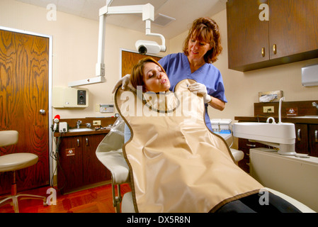 Zahnmedizinische Fachangestellte in Scrubs passt eine Bleischürze Sicherheit an einen Patienten vor der Durchführung einer Röntgenkontrolle auf ihre Zähne in Newport Beach, Kalifornien. Stockfoto