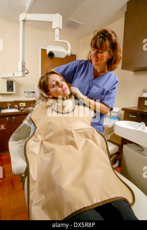 Zahnmedizinische Fachangestellte in Scrubs passt eine Bleischürze Sicherheit an einen Patienten vor der Durchführung einer Röntgenkontrolle auf ihre Zähne in Newport Beach, Kalifornien. Stockfoto