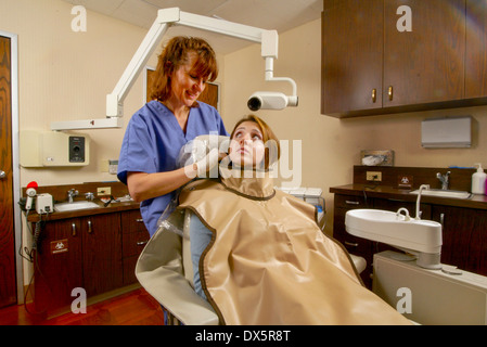 Zahnmedizinische Fachangestellte in Scrubs passt eine Bleischürze Sicherheit an einen Patienten vor der Durchführung einer Röntgenkontrolle auf ihre Zähne in Newport Beach, Kalifornien. Stockfoto