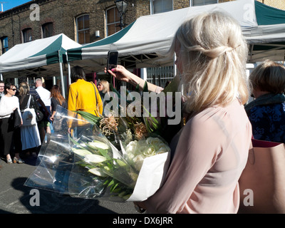 Eine Frau mit weißen Blumen in Columbia Road Blumenmarkt während der Einnahme eines selfie mit Handy London E2 UK KATHY DEWITT Stockfoto