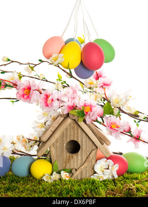 bunte Oster-Deko mit Vogelhaus und Eiern auf dem grünen Rasen. Frühjahr Apfel- und Kirschbäumen blüht Stockfoto