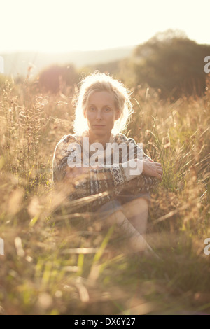 Eine junge Frau sitzt in einem Feld Gras mit der schwindenden dunstige Sonne hinter Stockfoto