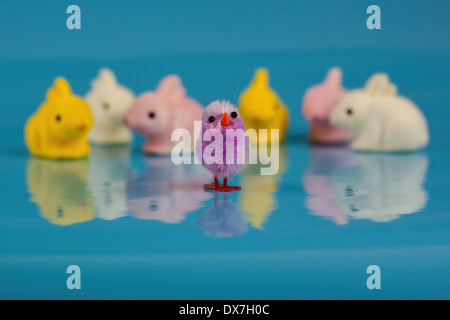 Ostern Küken Spielzeug, Lavendel Küken auf einem blauen glänzenden Hintergrund mit wenig Ostern Kaninchen und Hase Spielzeug im Hintergrund Stockfoto