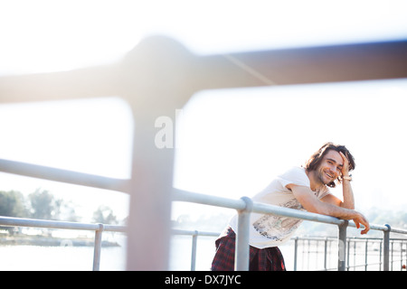 Ein gesundes und glückliches junger Mann stützte sich auf Geländer in der Nähe von Wasser Stockfoto