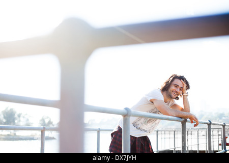 Ein gesundes und glückliches junger Mann stützte sich auf Geländer in der Nähe von Wasser Stockfoto