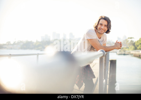 Ein gesundes und glückliches junger Mann stützte sich auf Geländer in der Nähe von Wasser Stockfoto