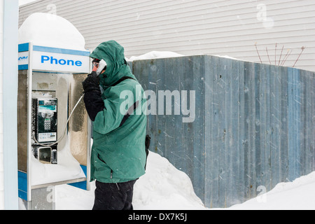 Ein Mann erzählt auf einem verschneiten Münztelefon im Schneesturm. Stockfoto