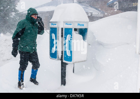 Ein Mann erzählt auf einem verschneiten Münztelefon im Schneesturm. Stockfoto