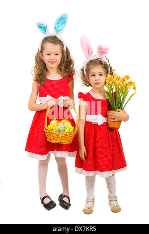 Schöne Schwestern in rot gekleidet, trägt Hasenohren und hält Korb mit Ostereier und Blumen isoliert auf weißem Hintergrund Stockfoto
