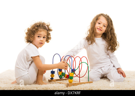 Glücklich zwei Mädchen spielen mit Holzspielzeug Home und sitzen zusammen auf Fell Teppich Stockfoto