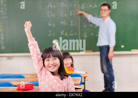 Schülerinnen und Schüler während des Unterrichts mit Lehrerin im Klassenzimmer Hände erhebend Stockfoto