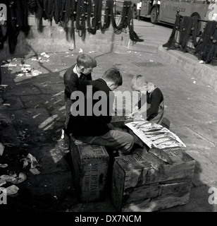 1950er Jahre, historische Bild von drei Jungen sitzen auf Holzkisten Schneiden von Fisch mit einem gewöhnlichen Tisch Messer, London. Stockfoto